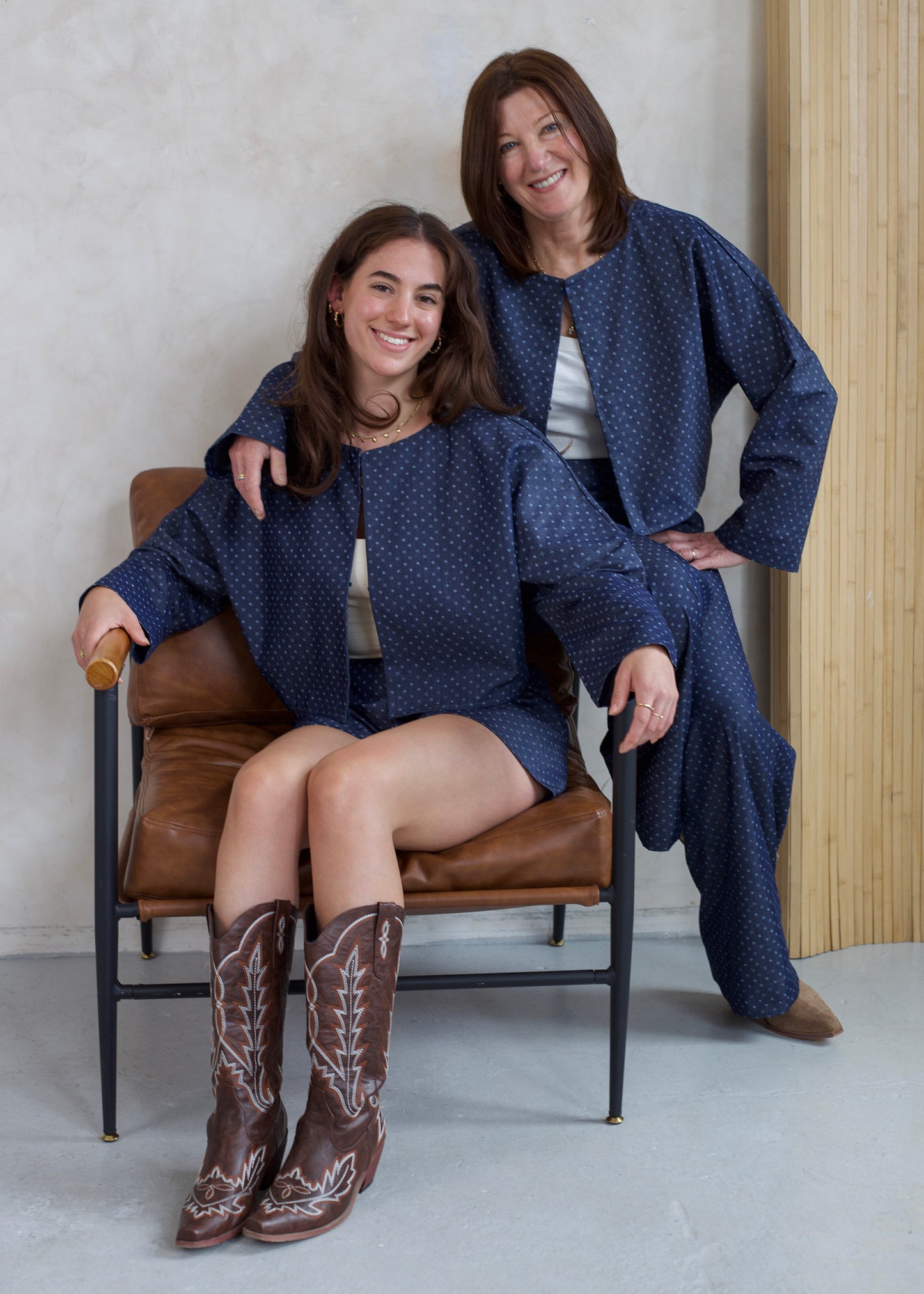 Two women in matching blue outfits with a brown chair and wooden floor.