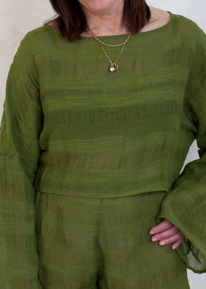 A person wearing a textured olive green two-piece set consisting of a long-sleeve top and matching shorts, accessorized with a gold chain necklace.