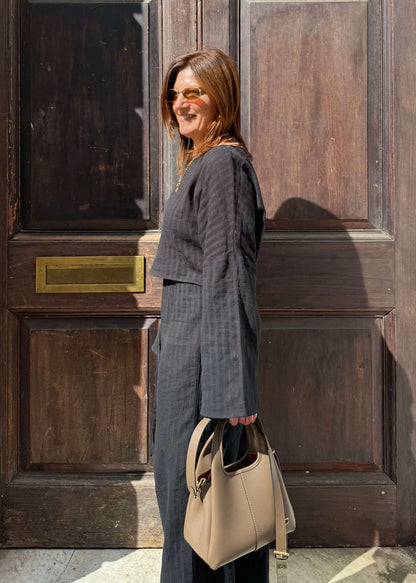 A woman stands in front of a dark wooden door, wearing a black striped two-piece set and holding a handbag.