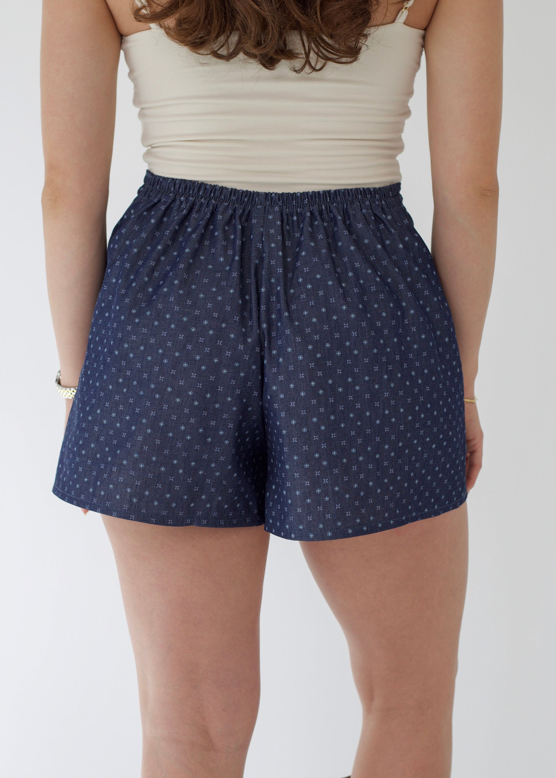 Person wearing navy blue shorts with white polka dots on a plain background