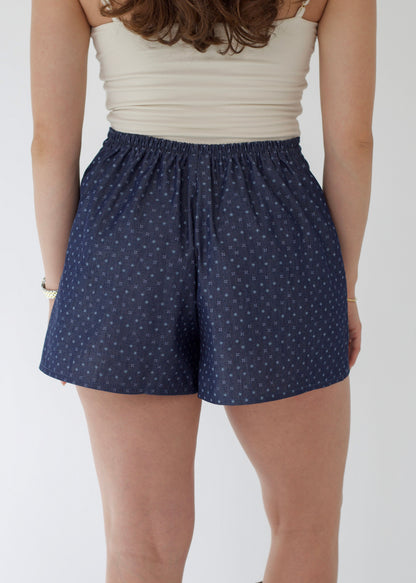 Person wearing navy blue shorts with white polka dots on a plain background