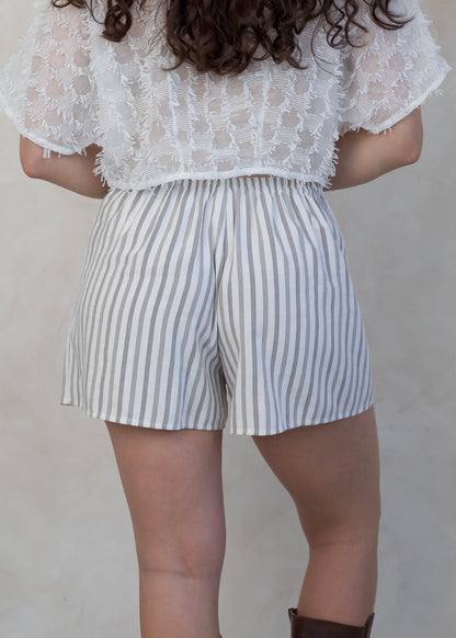 Person wearing a white lace top and striped shorts on a plain background