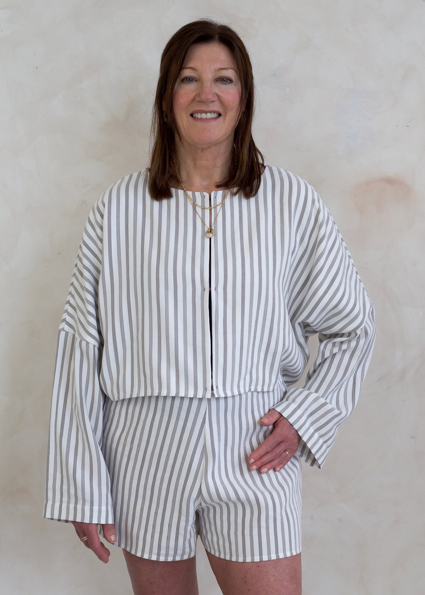 Woman wearing a white and brown striped outfit against a beige wall