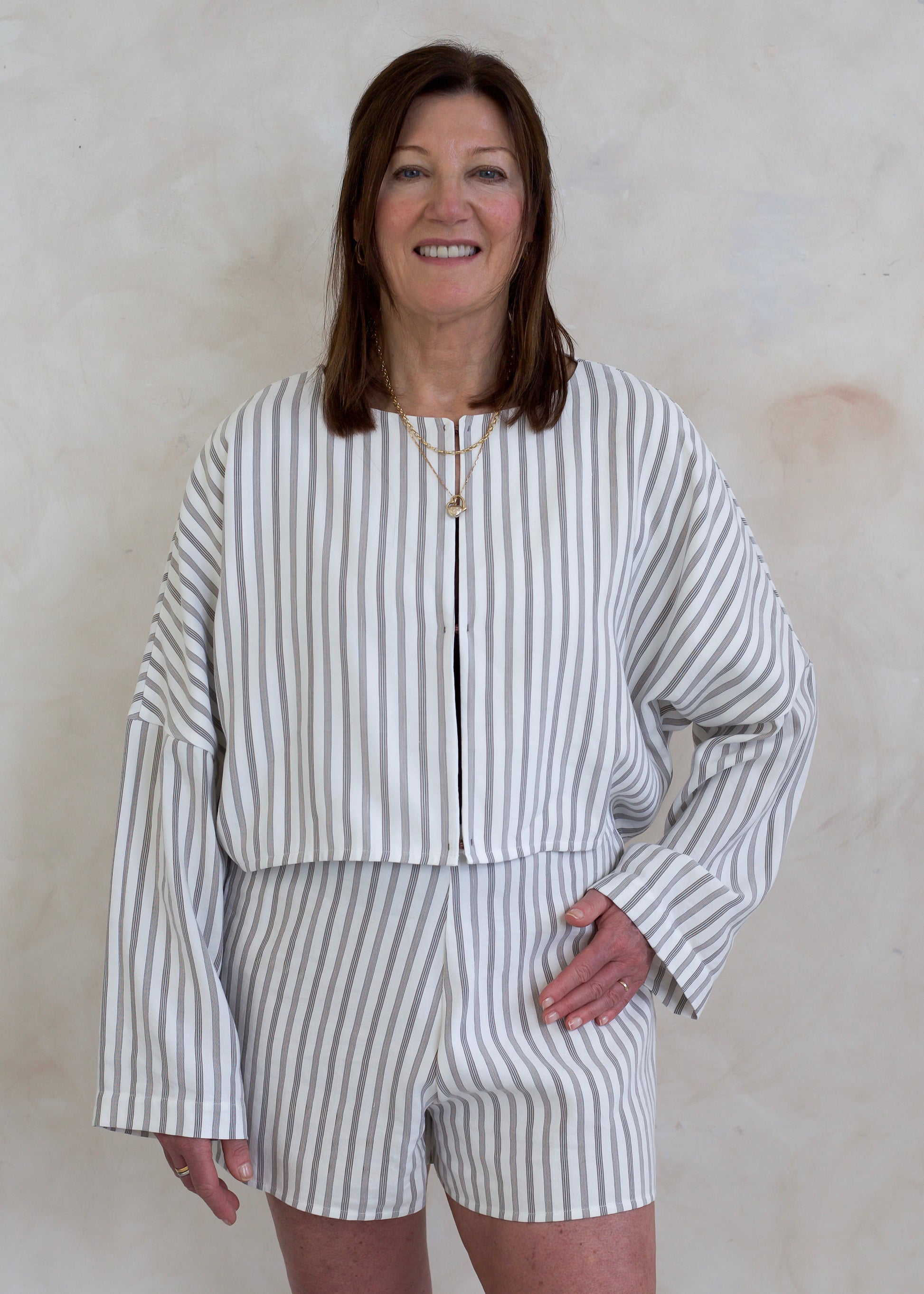 Woman wearing a white and brown striped outfit against a beige wall