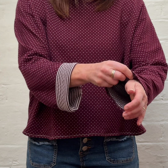 Video shows a woman folding the sleeves of a burgundy knit to reveal a striped pattern.
