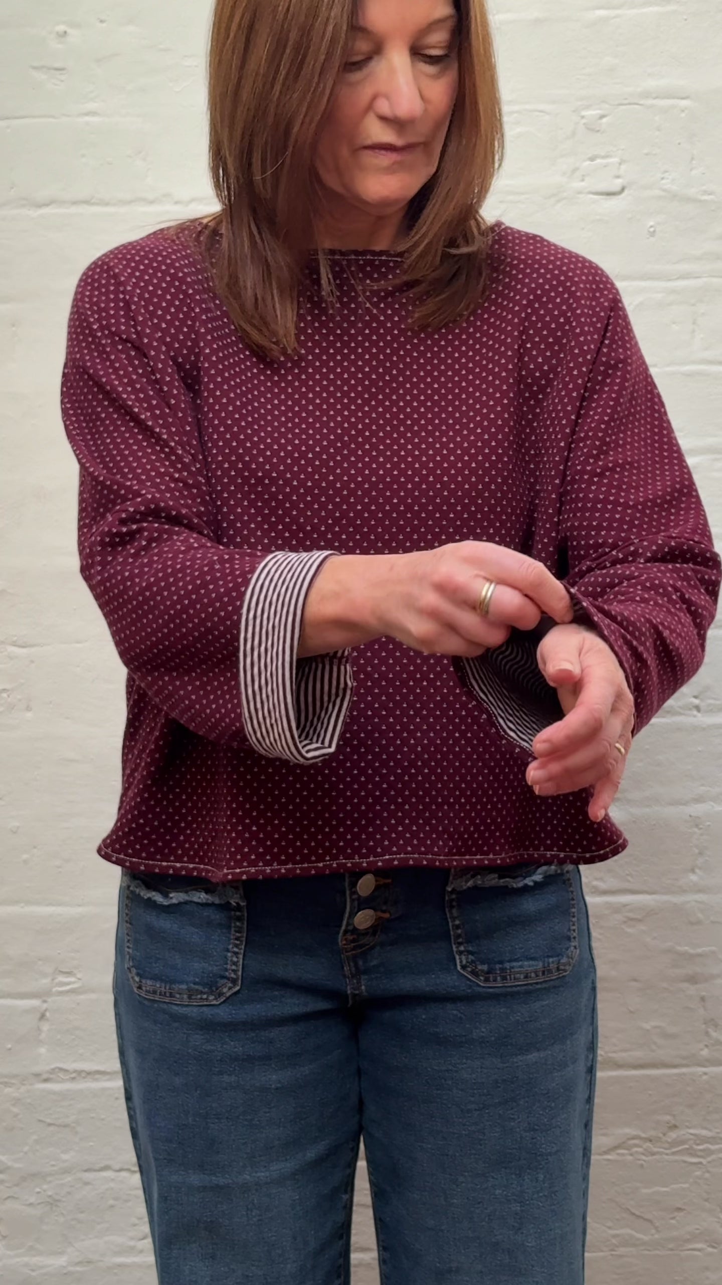 Video shows a woman folding the sleeves of a burgundy knit to reveal a striped pattern.